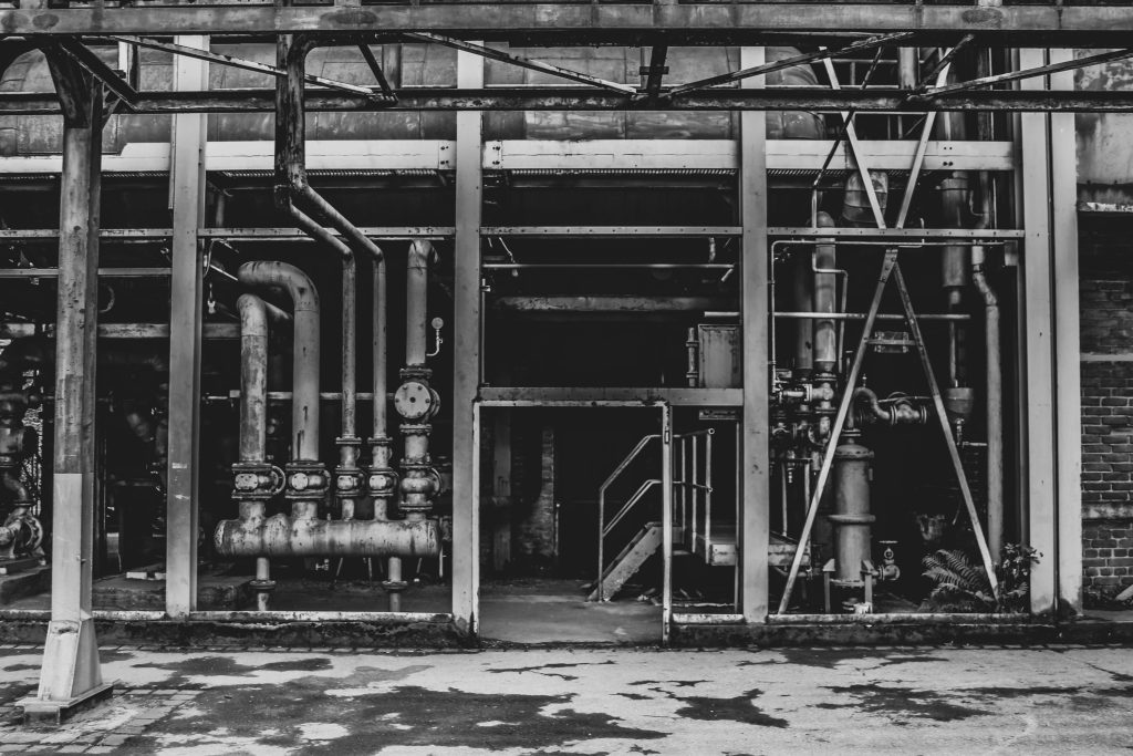 pexels photo 1472237 1472237 A black and white photo of an abandoned industrial building with exposed pipes and steel structures.